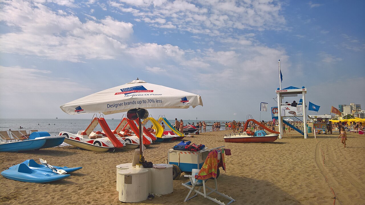Panoramica della spiaggia di Jesolo a fine mattinata, con ombrelloni colorati allineati e bagnanti rilassati sotto un cielo sereno